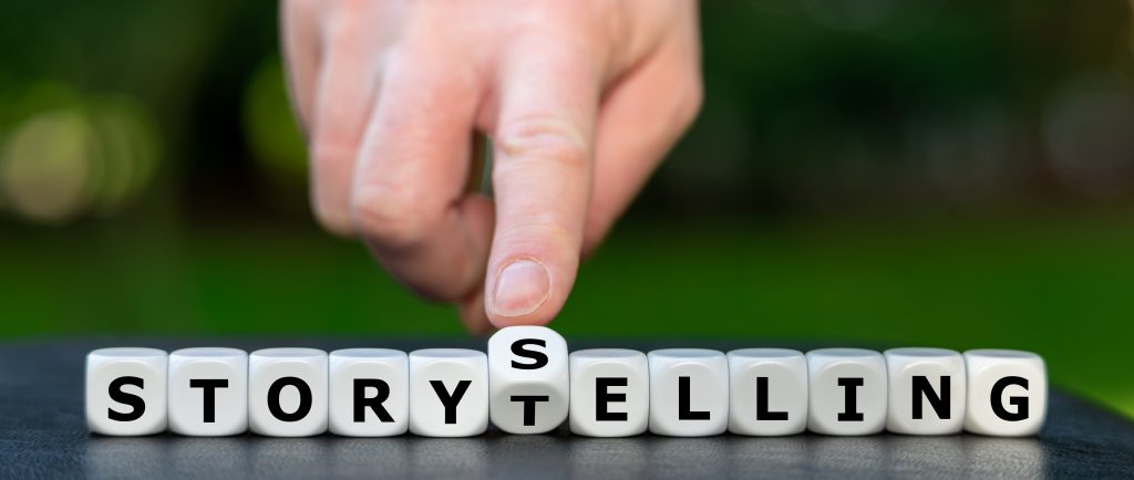 A row of block letters with a man's hand tilting one letter in the middle so that there are present the words "storytelling" and "storyselling" simultaneously.
