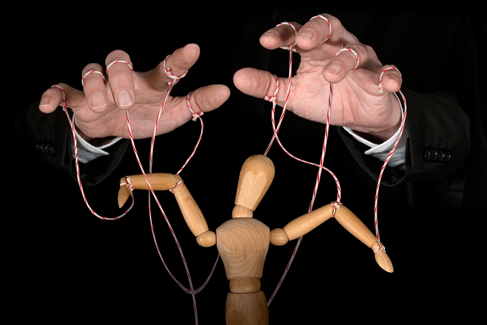 Hands moving a marionette (a wooden doll) as a visual metaphor of consumer manipulation through branding.