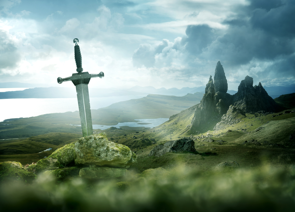 An aged knights sword stuck in the ground with the rolling mountains from the Isle of Skye in the background. Fantasy 3D mixed media illustration.